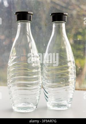 Two empty clear glass bottles with black caps sit on a white surface Stock Photo