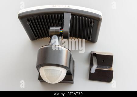 A black motion sensor LED floodlight with its bracket on white Stock Photo