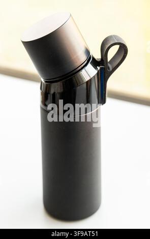 A sleek black insulated bottle stands on a clean white surface Stock Photo