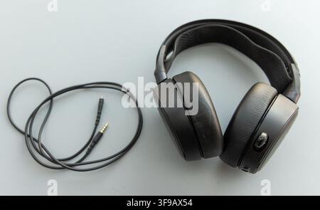Black overear headphones and a coiled audio cable lie on a gray surface Stock Photo