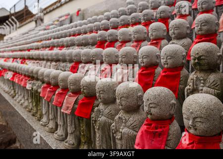 A close up perspective view of hundreds of stone Jizo statues with red bibs arranged on tiers at Shitennoji temple in Osaka Japan. Stock Photo