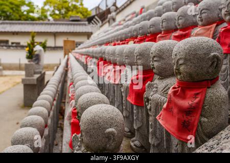 A close up perspective view of hundreds of stone Jizo statues with red bibs arranged on tiers at Shitennoji temple in Osaka Japan. Stock Photo