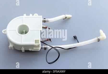 A white plastic component with attached hoses and wires rests on a gray surface Stock Photo