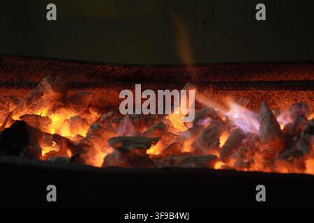 A glowing barbecue grill with burning charcoal, glowing red embers, and small purple-blue flames. Perfect texture shot for outdoor grilling background. Stock Photo