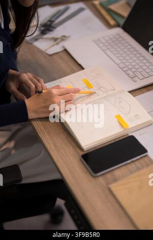 Female furniture designer working on technical sketches and blueprint plans with digital tools at modern office desk Stock Photo