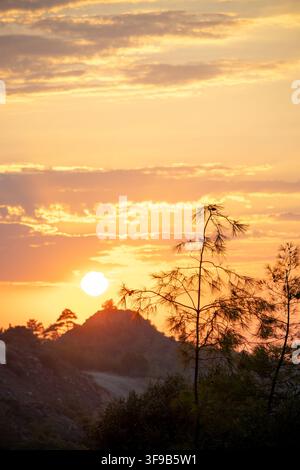 Karmi. Karmi village. North Cyprus. Bright sun setting over a scenic mountain landscape, silhouetting pine trees under a warm golden and orange sky Stock Photo
