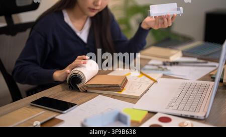 Professional designer examining fabric swatches and architectural plans on wooden desk during creative workflow Stock Photo