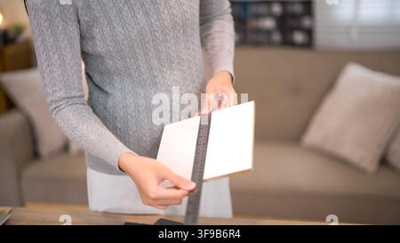 Female designer measuring and selecting white material swatches for custom furniture project in creative home workshop Stock Photo