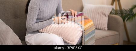 Female designer examining fabric samples and paint chips while planning home decor renovation seated on sofa Stock Photo
