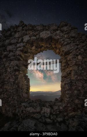 View of the Milky Way framed by the ancient stone window of the Rocca Calascio ruins at night in Calascio, Abruzzo, Italy. Stock Photo
