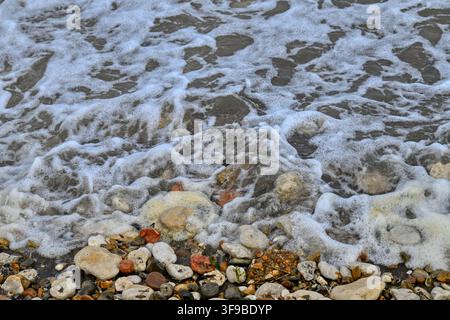 Abstract of a calm sea with a little foam lapping on a beach with sand and pebbles Stock Photo
