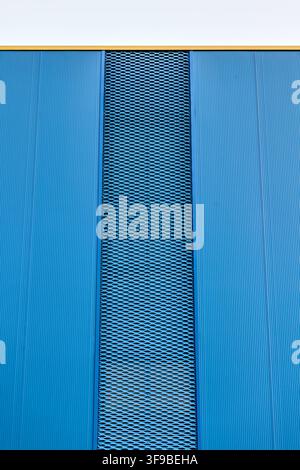 Vertical strip of blue expanded metal mesh set between corrugated metal wall panels Stock Photo