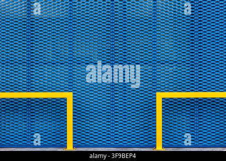 Blue expanded metal mesh wall with two yellow pipe railings mounted at the base Stock Photo