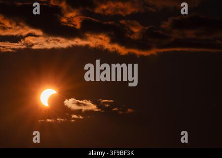 View of a partial solar eclipse partially obscured by dark, dramatic clouds during sunset in Merikula, Harju maakond, Estonia. Stock Photo