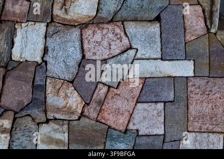 Mosaic pattern of angular flagstone pieces in varied colours forming a textured stone wall Stock Photo