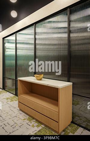 A contemporary hallway or office interior featuring a textured fluted glass partition with black metal framing. A light wood storage console. Stock Photo