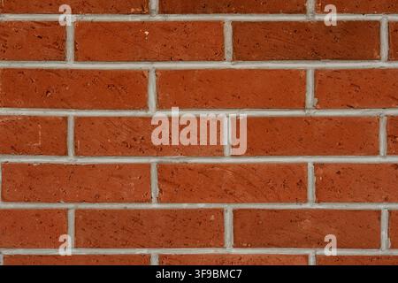 A close-up background texture of a newly constructed red clay brick wall featuring rough surfaces and clean white mortar joints in a running bond. Stock Photo