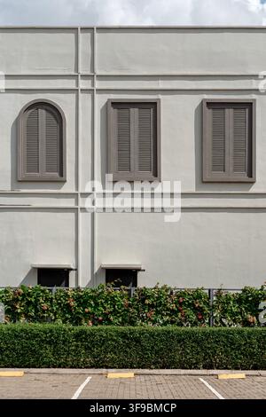 A straight-on architectural exterior view of a smooth white building facade featuring decorative molding lines, one arched louvered window, two rectan Stock Photo