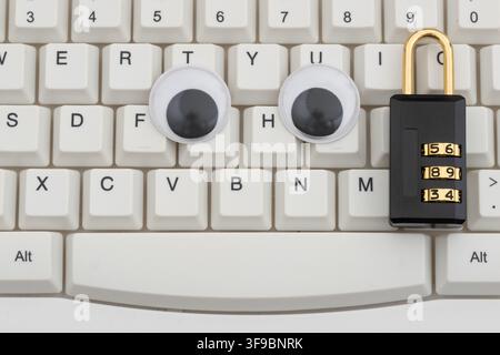 Googly eyes with combination lock on a white computer keyboard for privacy protection Stock Photo