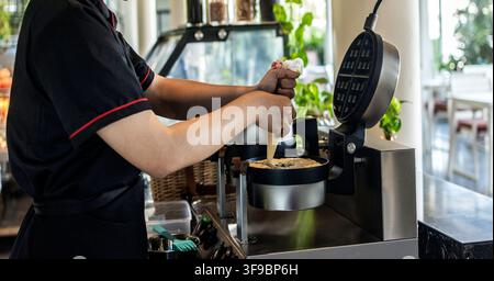 kitchen staff making fresh waffles in professional modern waffle cooking machine at outdoor cafe Stock Photo
