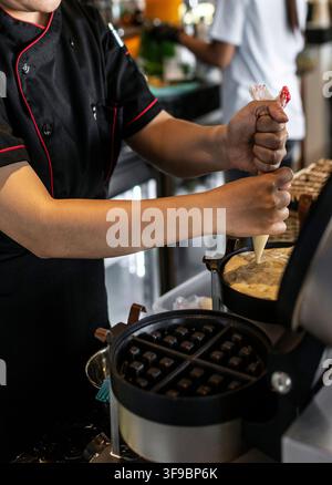 kitchen staff making fresh waffles in professional modern waffle cooking machine at outdoor cafe Stock Photo