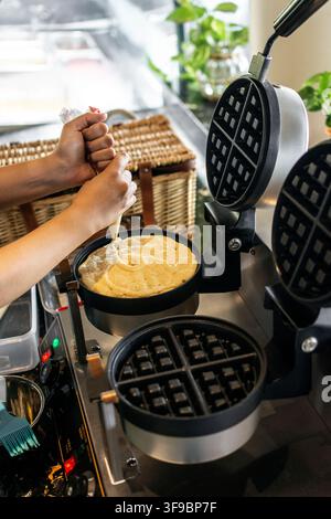kitchen staff making fresh waffles in professional modern waffle cooking machine at outdoor cafe Stock Photo