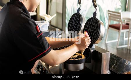 kitchen staff making fresh waffles in professional modern waffle cooking machine at outdoor cafe Stock Photo