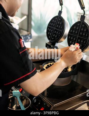 kitchen staff making fresh waffles in professional modern waffle cooking machine at outdoor cafe Stock Photo