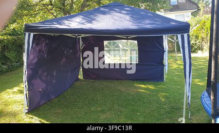 A child peeks out from a blue popup tent on a sunny lawn Stock Photo