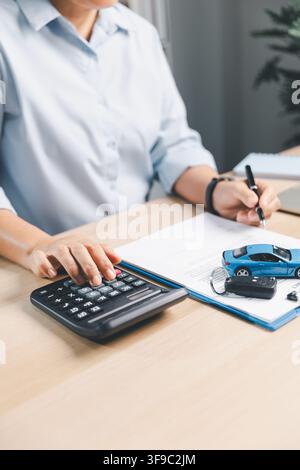 Business person calculating and signing vehicle finance documents with blue toy car, calculator, and car key, representing auto loan, car insurance, a Stock Photo