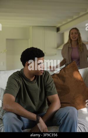 Diverse couple sitting on light sofa with brown pillow, man wearing wristband, woman speaking Stock Photo