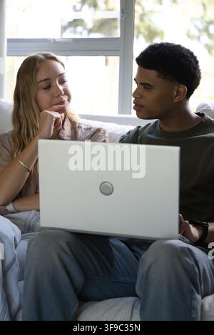 Couple sitting on sofa near window at home, woman with bracelet, man with wristwatch using laptop Stock Photo
