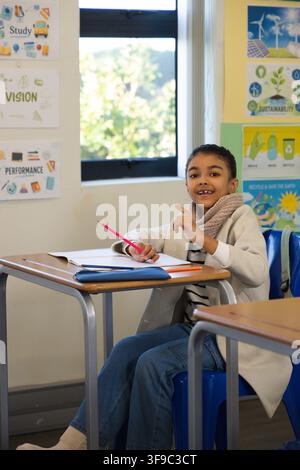 Female child student sitting at desk in classroom writing in open notebook with red pencil Stock Photo