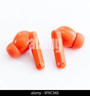 Two vibrant orange wireless earbuds rest on a clean white surface Stock Photo