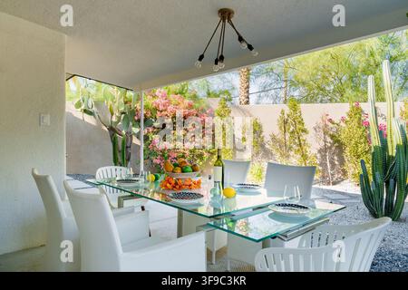 A beautifully set outdoor dining table under a covered patio. Lush greenery and a relaxed atmosphere. Stock Photo