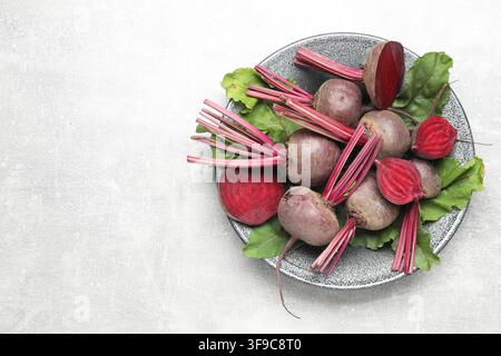 Whole and cut young beets with green leaves on gray textured table, top view. Space for text Stock Photo