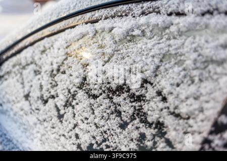 Close-up of a car window covered in snowflakes, showcasing the intricate patterns and textures of frost on the glass surface Stock Photo