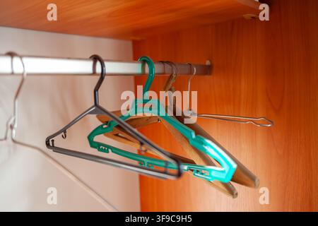 Colorful plastic and metal hangers hanging on a clothes rack inside a wooden closet with a smooth surface and warm lighting Stock Photo