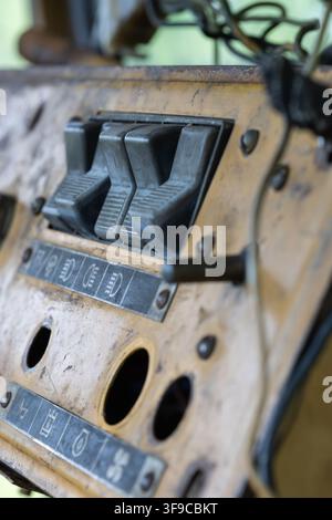 weathered yellow dashboard of an abandoned vehicle, featuring a black control switch, an empty gauge hole, peeling paint, and surface rust. Stock Photo