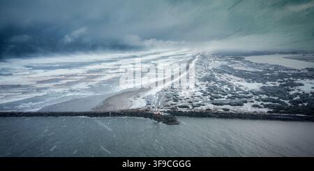 Aerial view of Coquille River Lighthouse at the mouth of the river, surrounded by stormy waves, snow-dusted coastline, and dark clouds in Bandon, Oreg Stock Photo