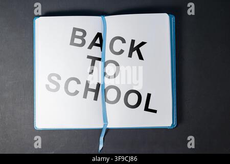 Top view of an open blue notebook with Back to School text on clean white pages over a dark wooden background. High Quality Photo Stock Photo