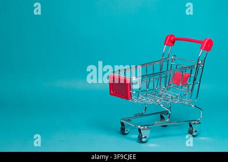 An empty small red metal shopping cart isolated on a vivid blue studio background with copy space. High Quality Photo Stock Photo