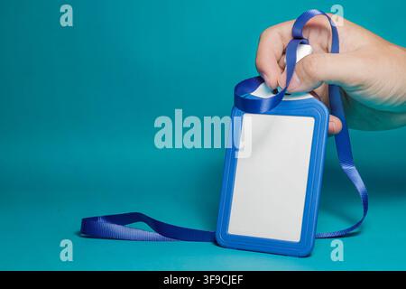 Close up of a hand holding an empty blue identification badge card with strap on blue background. High Quality Photo Stock Photo