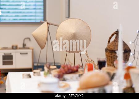 Vietnamese cultural display at European event featuring traditional conical hats non la, bamboo basket and Vietnamese cuisine on table with modern kitchen background Stock Photo