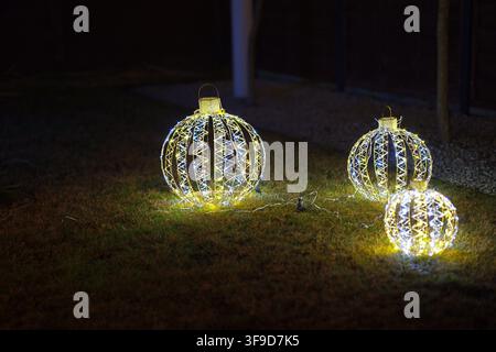 A close-up view of illuminated Christmas ornaments glowing on a grassy ground level, supported by metal wire, creating a festive outdoor lighting scen Stock Photo