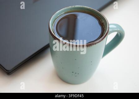 cup of black tea on the table next to the laptop Stock Photo