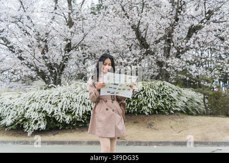 Young female traveler checking a map beneath cherry blossom blooming in garden during springtime at Japan Stock Photo