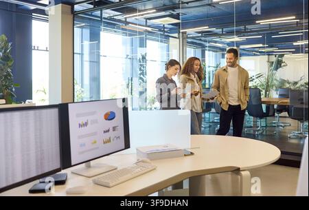 Colleagues discussing reports in a modern office, analytics on computer screens Stock Photo