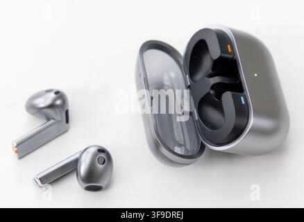 Two grey wireless earbuds rest beside their open charging case Stock Photo