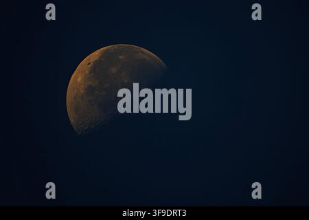 Detailed lunar surface emerges between drifting clouds during quiet twilight observation outdoors Stock Photo